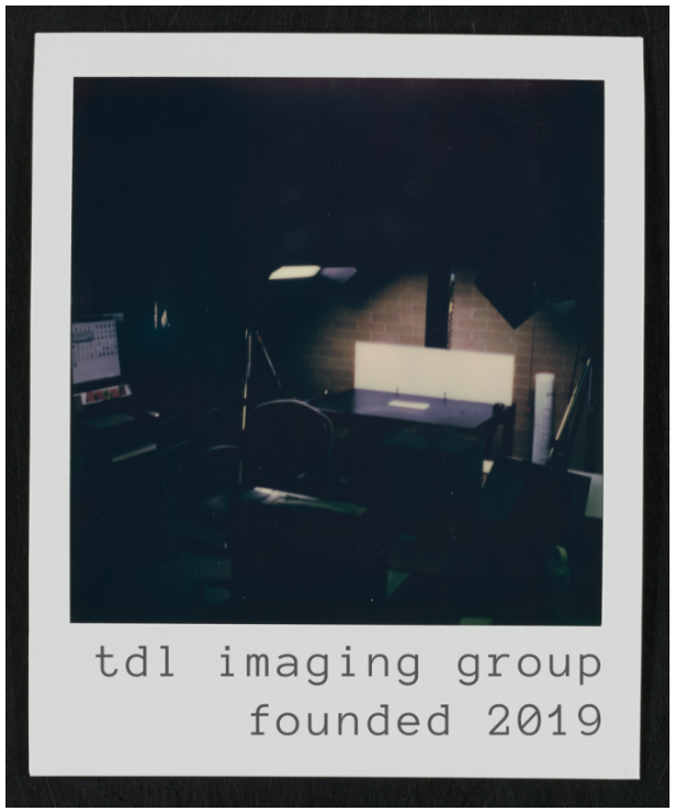 Dimly lit photo of a digitization station, with the overhead lights on. Below the image is the caption “tdl imaging group, founded 2019.”